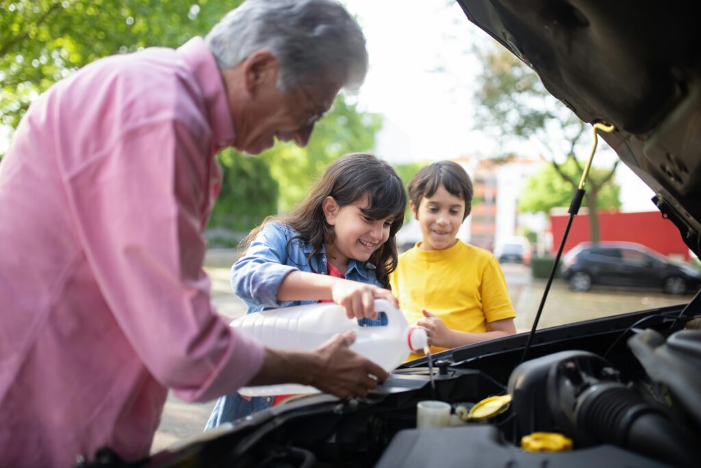 relaciones intergeneracionales, un sueño mayor enseñando a dos jóvenes como poner agua refrigerante en el coche